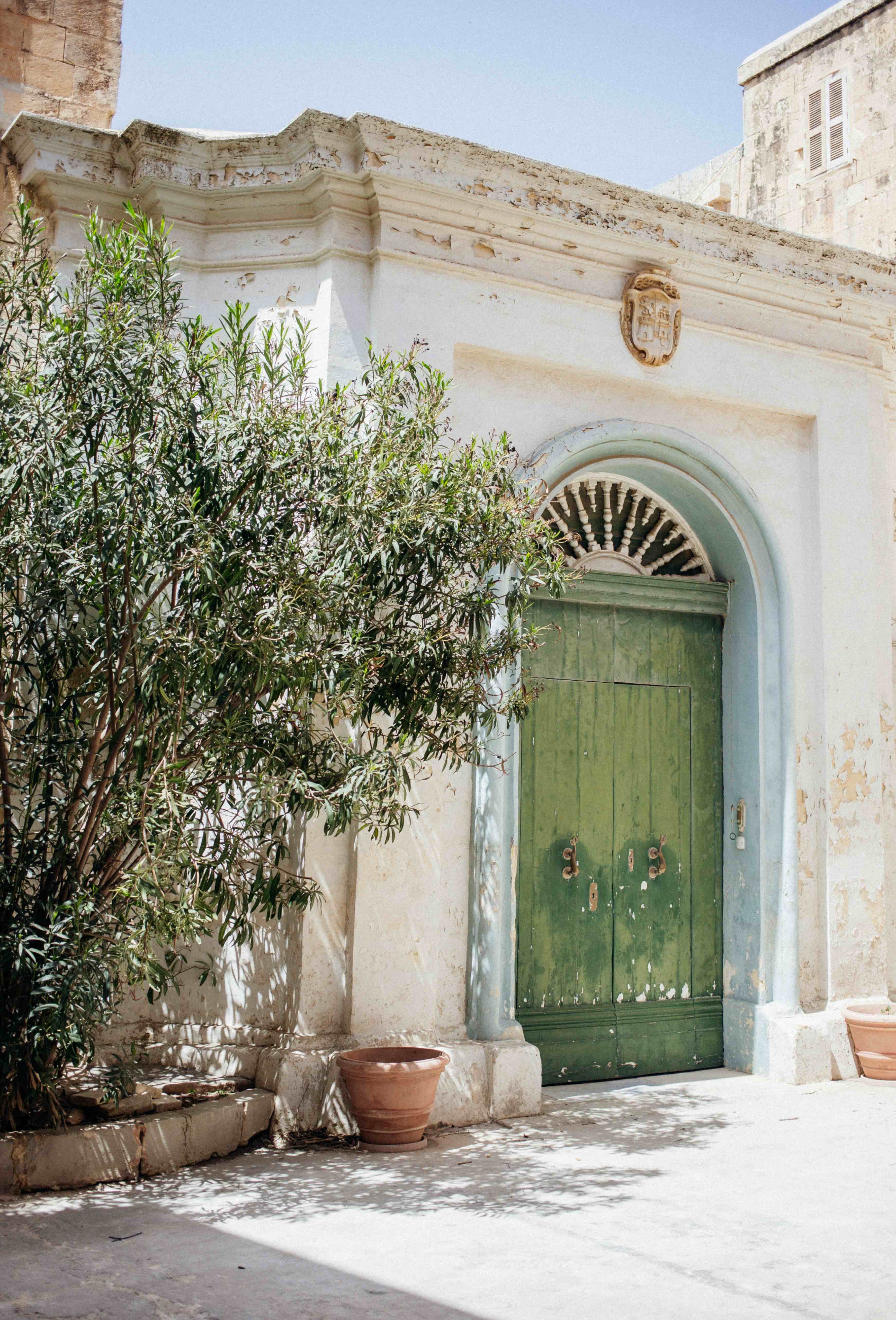 Maltese limestone courtyard with green arched door and olive tree — Mediterranean living