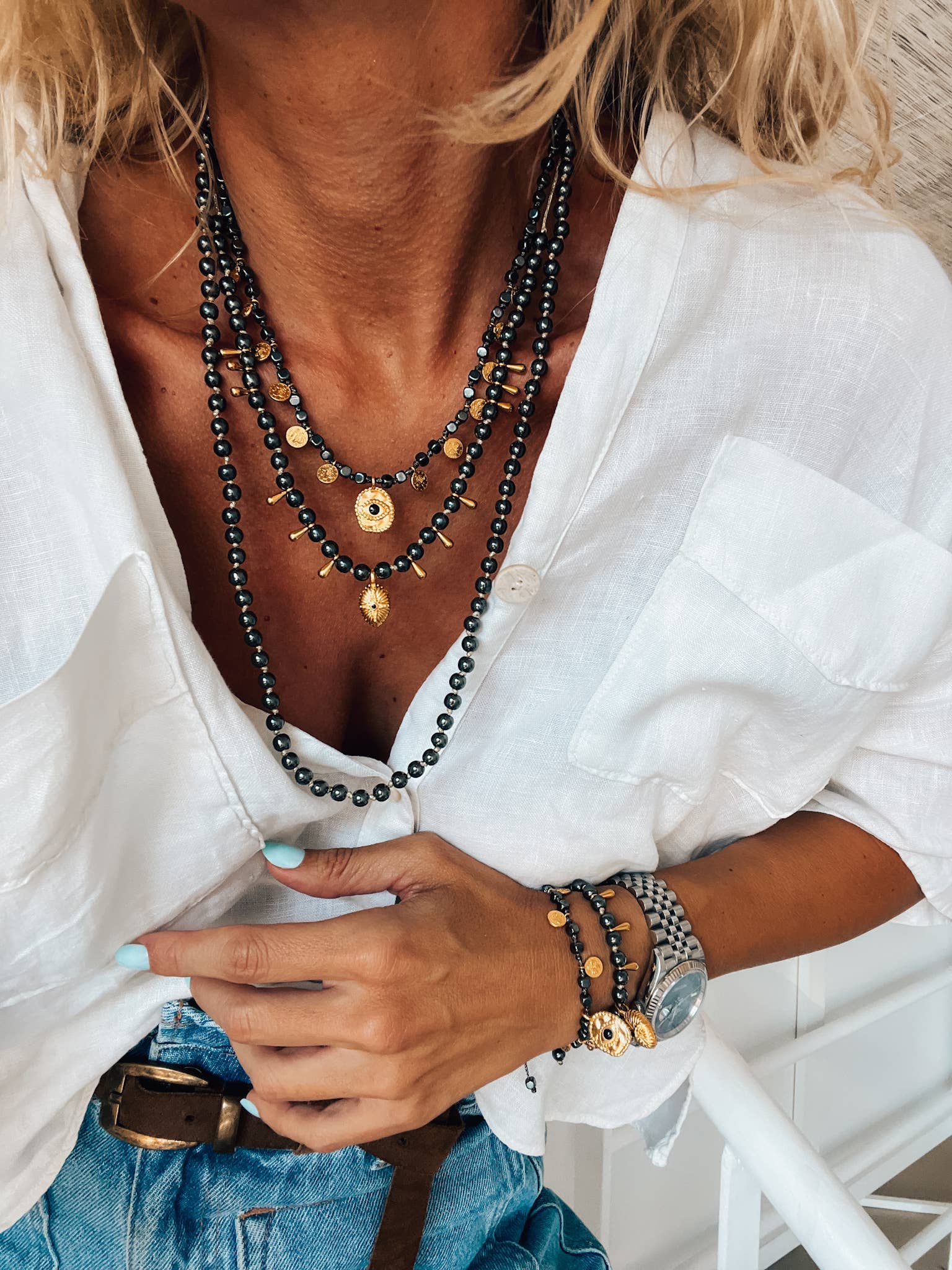 Black hematite and gold charm necklace worn at the collarbone over a white shirt.