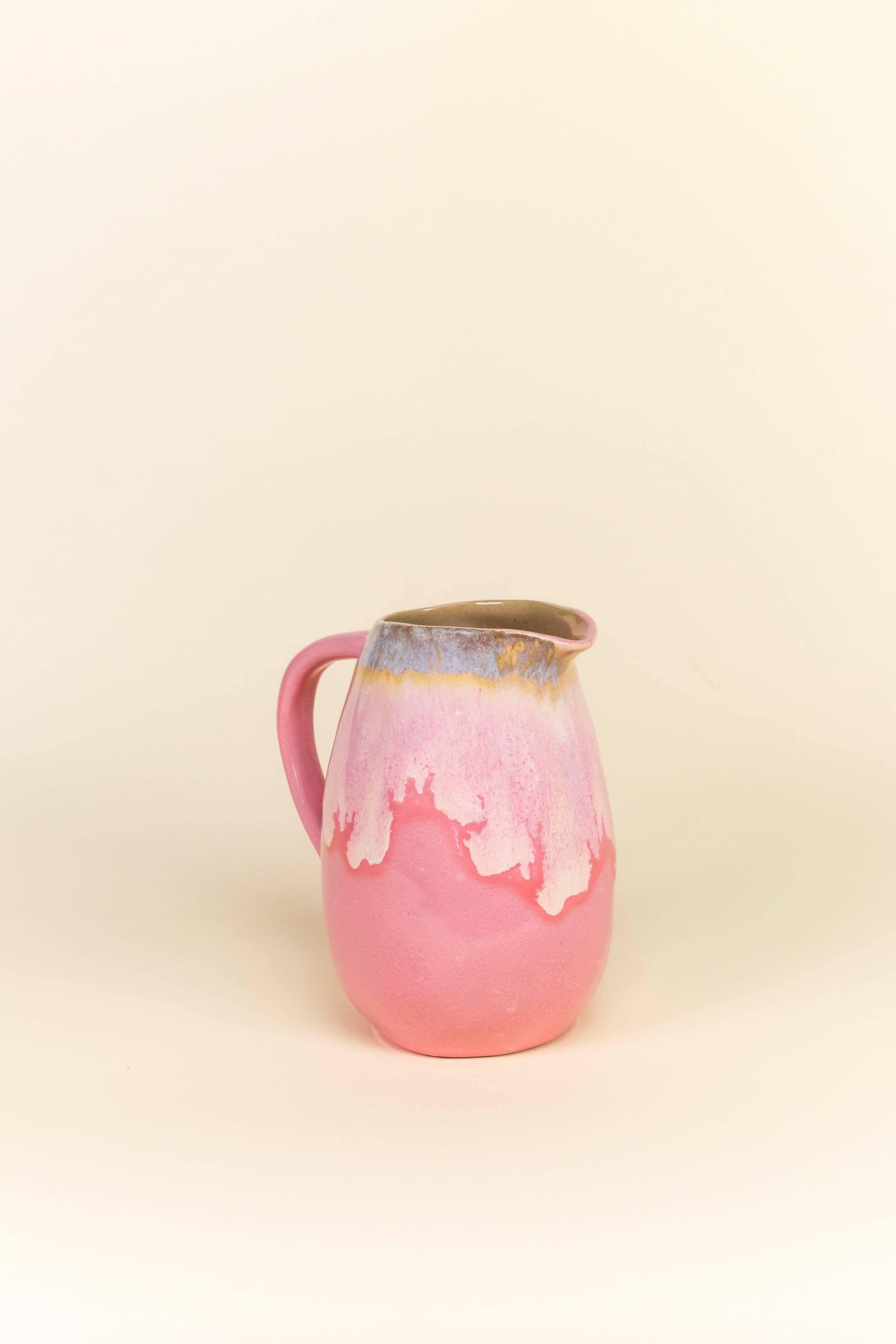 Pink ceramic pitcher with a gold rim on a beige background