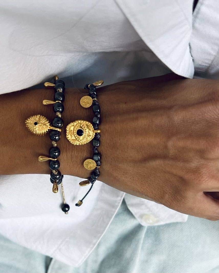 Black beaded bracelet with gold accents on a wrist against a white shirt background