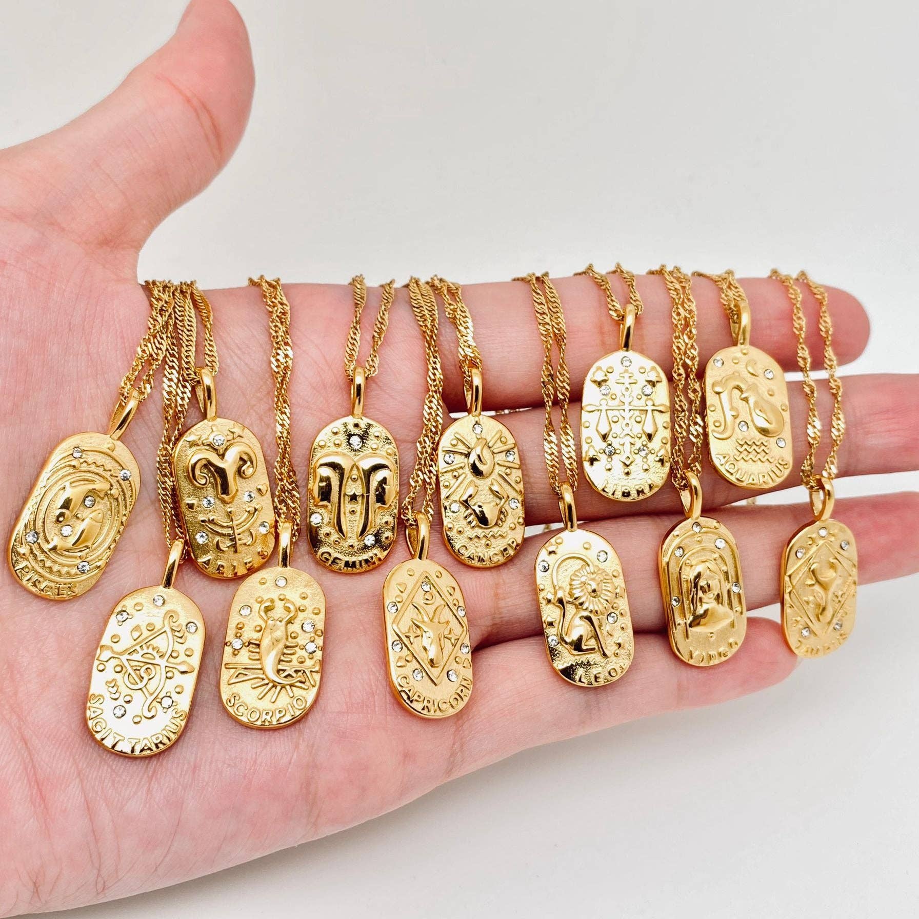 Hand holding multiple gold necklaces with various pendants on a light background