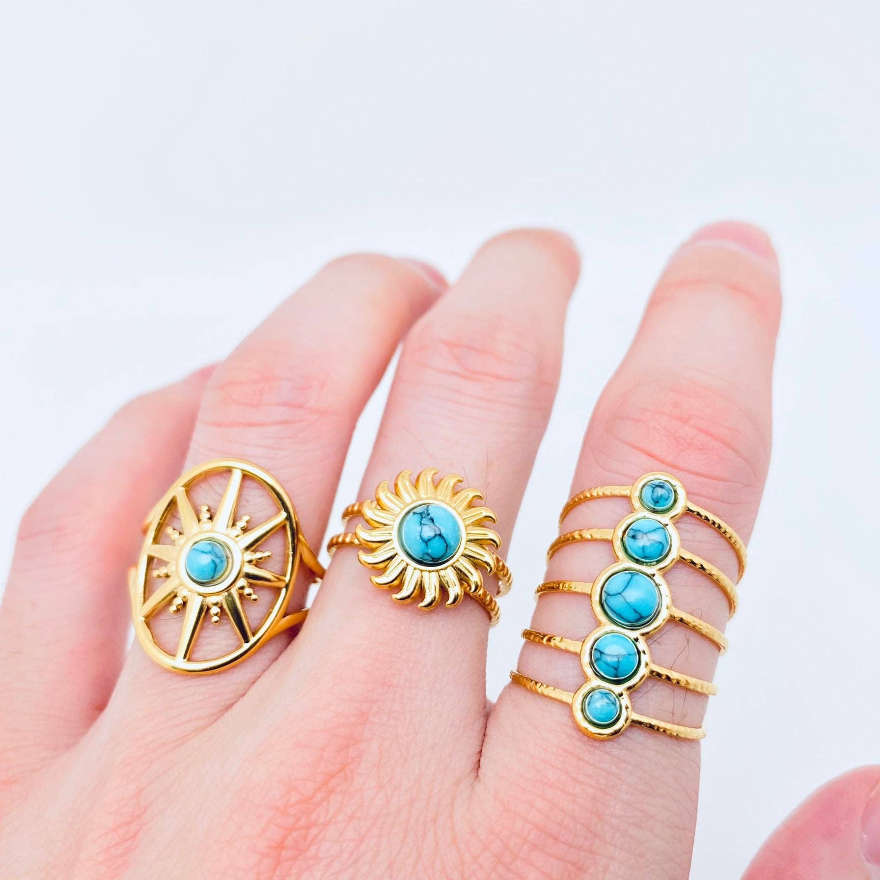 Hand wearing multiple gold rings with turquoise stones on a light background