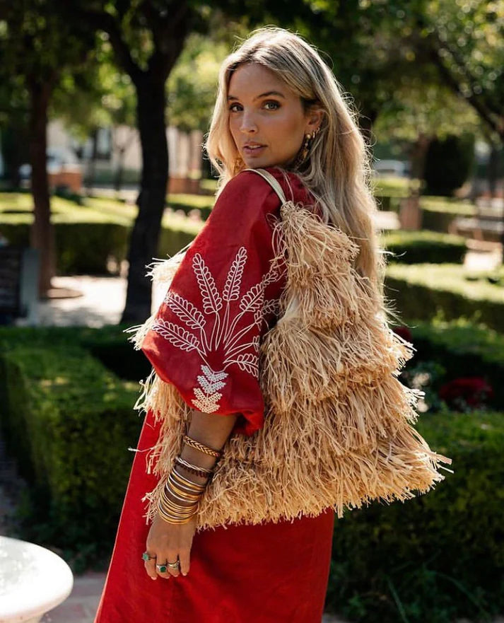Woman carrying a natural raffia fringe shoulder bag over one shoulder.

