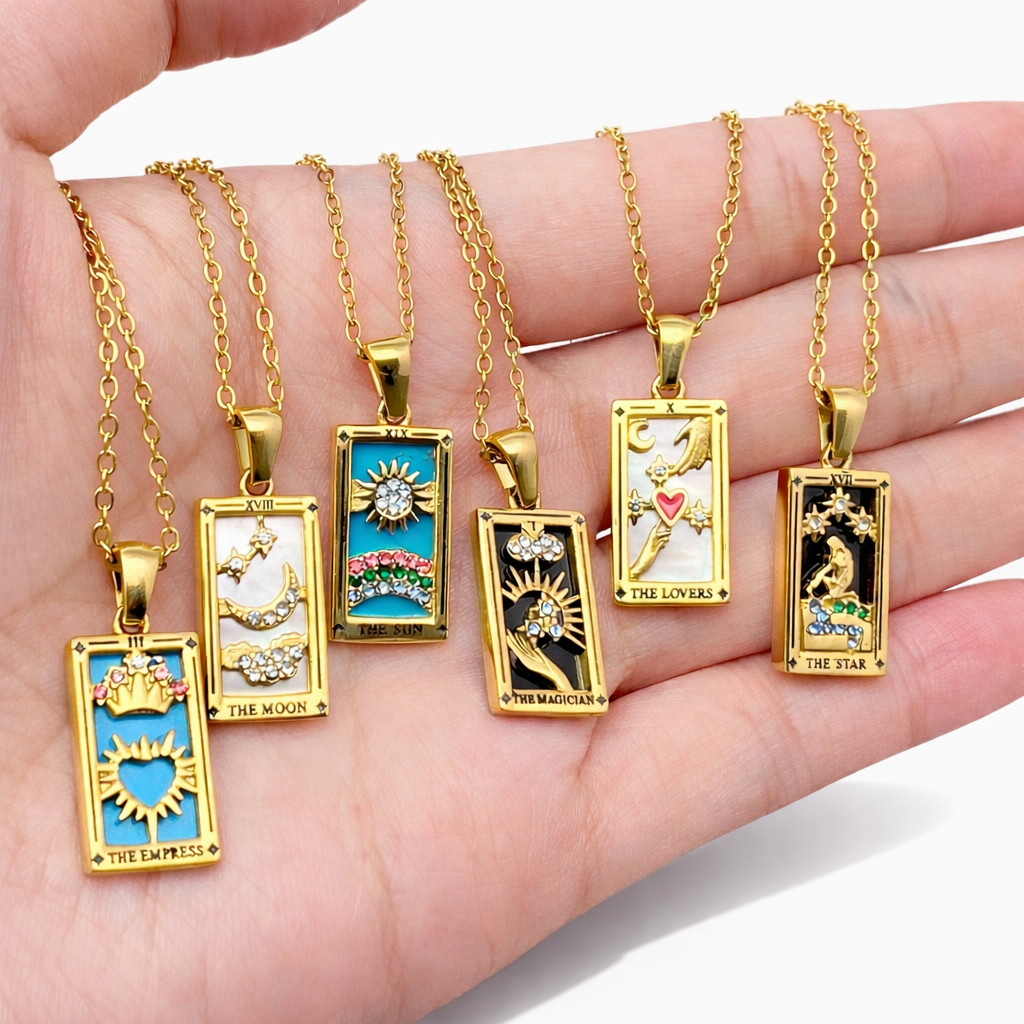 Gold tarot card pendants on chains held in a hand against a white background